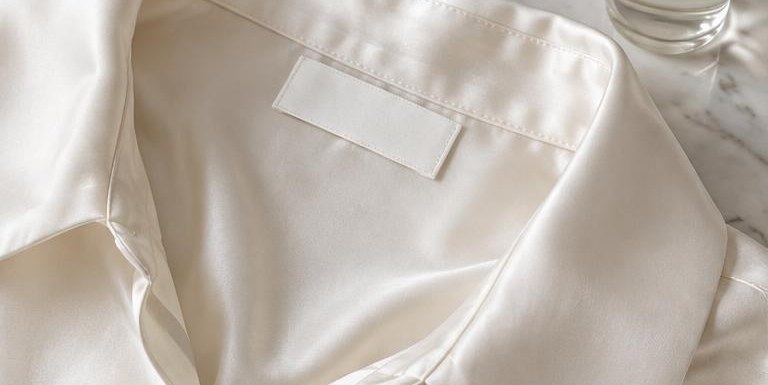 The collar of a cream silk shirt with a blank care label beside a small bottle