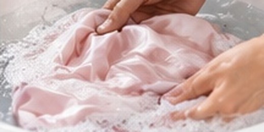 Hands gently washing pink silk in a basin
