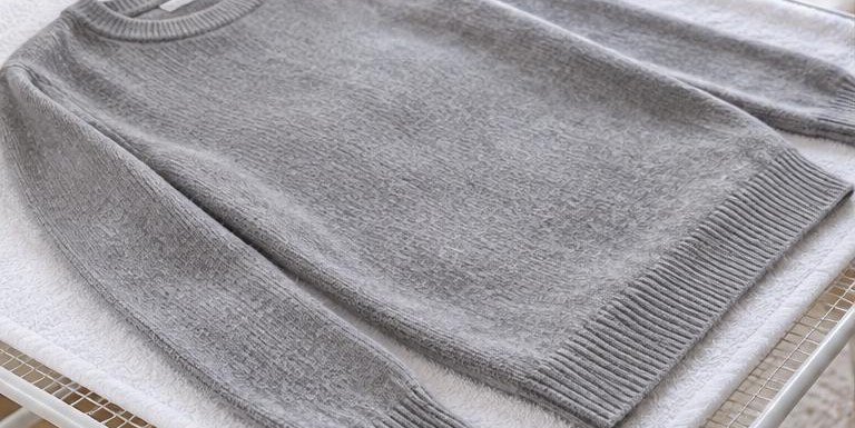 A grey cashmere sweater laid flat to dry on a white towel over a drying rack
