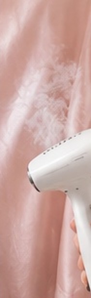 A garment steamer releasing steam over pink silk